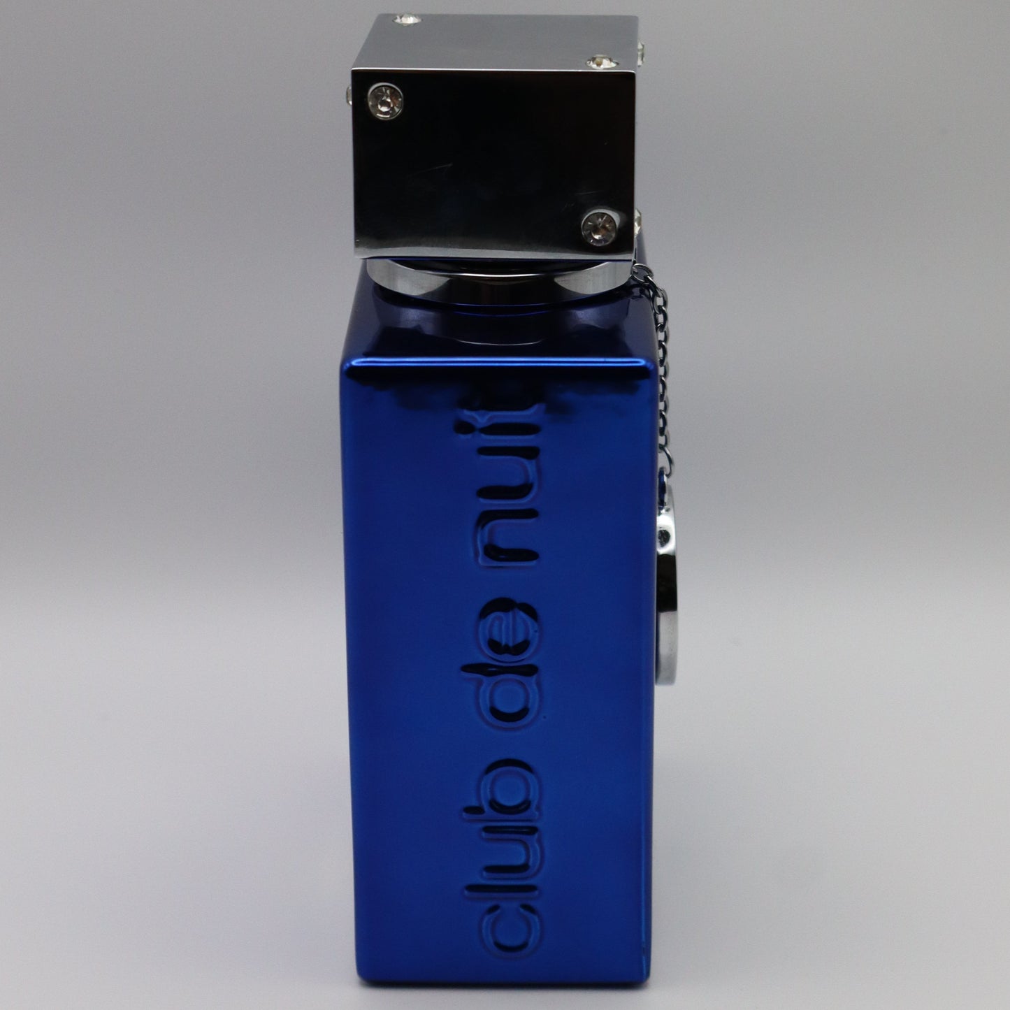 A blue metal perrfume bottle with a silver top, featuring the vertical text 'club de nuit' embossed. The bottle is shown from a side profile view on a neutral gray background.