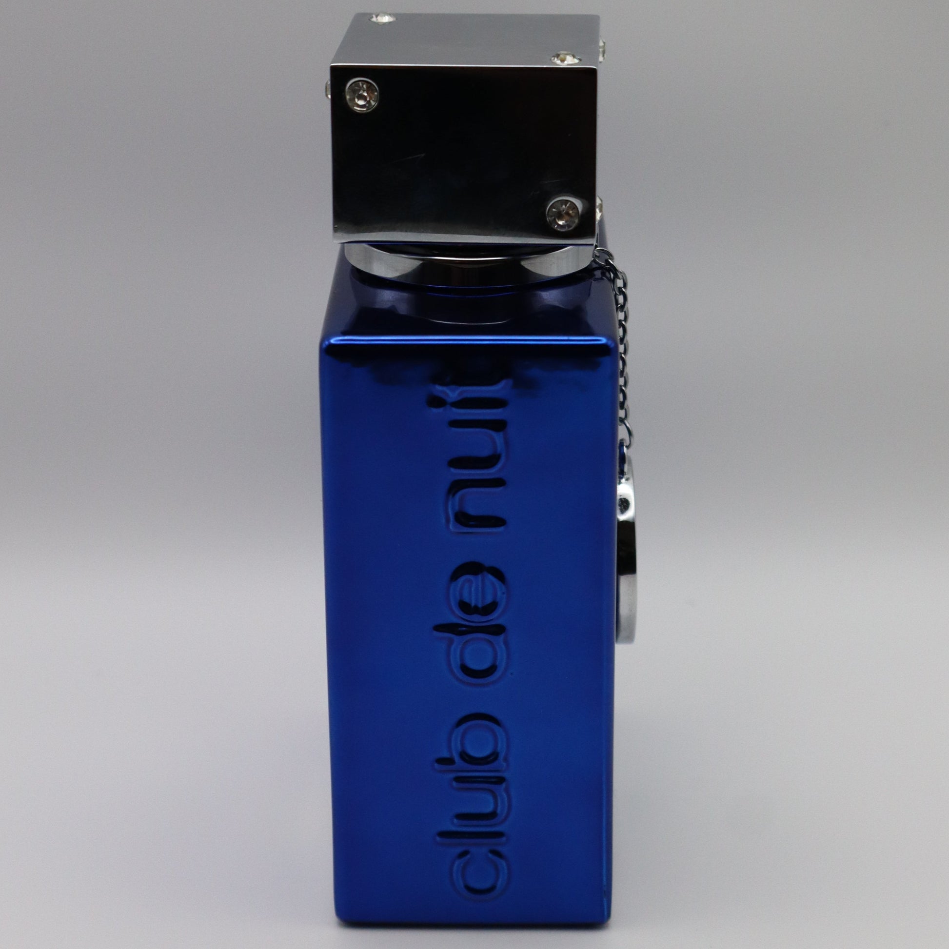 A blue metal perrfume bottle with a silver top, featuring the vertical text 'club de nuit' embossed. The bottle is shown from a side profile view on a neutral gray background.