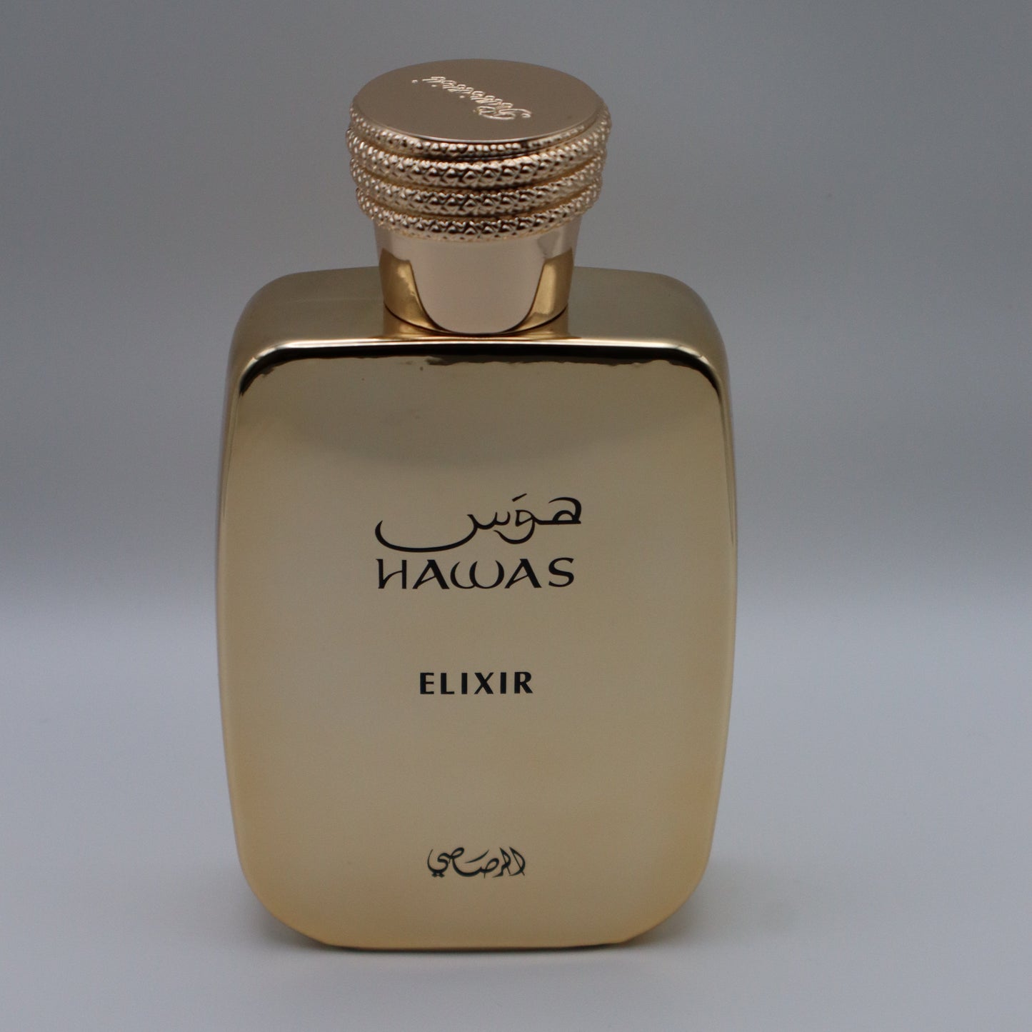 Metallic gold-colored rectangular perfume bottle with text that reads 'HAWAS', 'ELIXIR' and arabic text, all under a textured gold cap