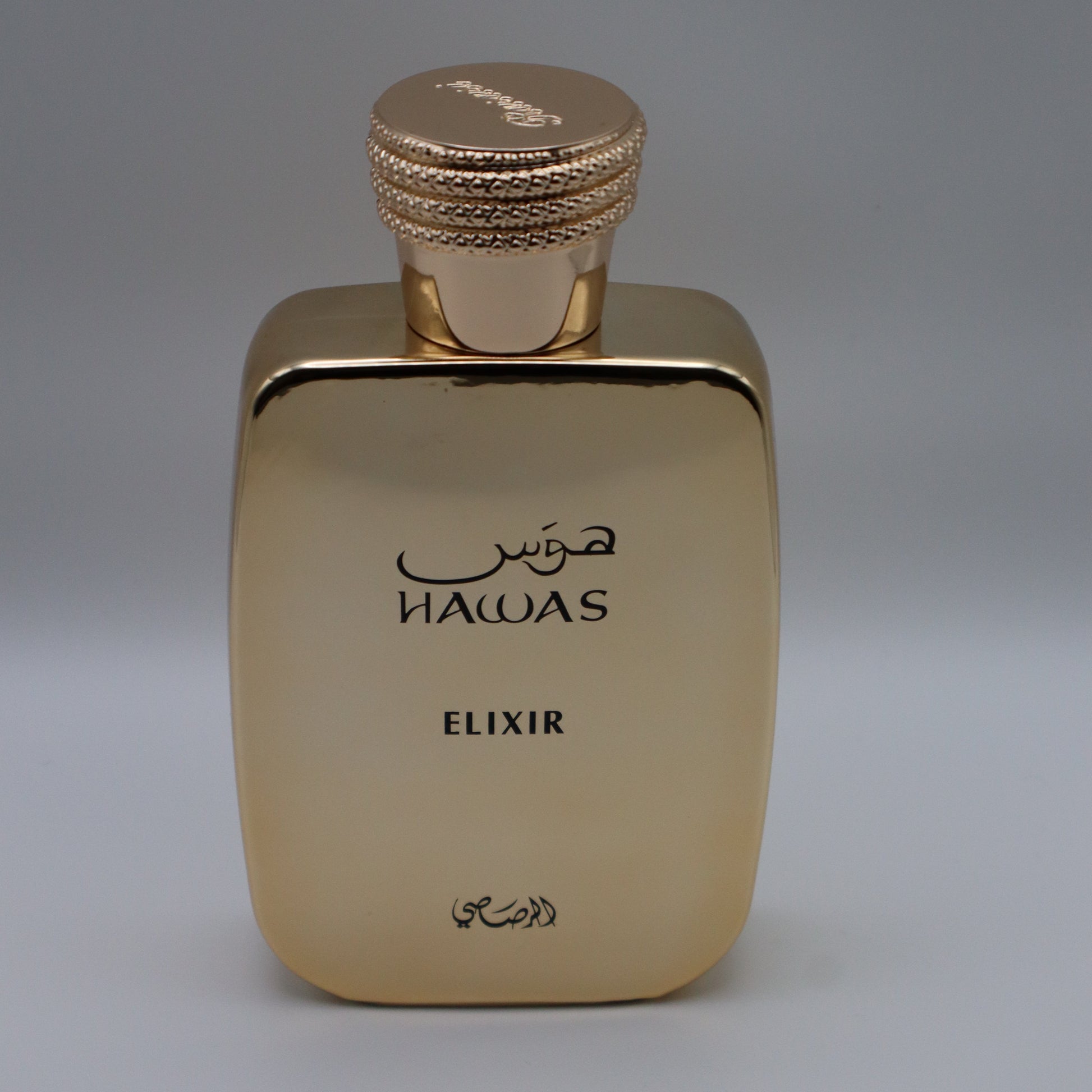Metallic gold-colored rectangular perfume bottle with text that reads 'HAWAS', 'ELIXIR' and arabic text, all under a textured gold cap