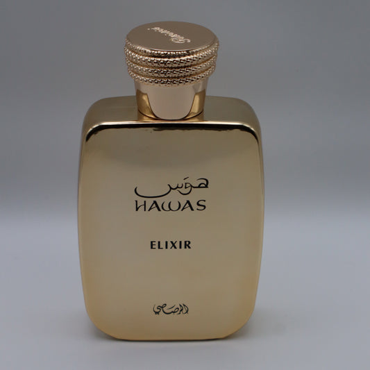 Metallic gold-colored rectangular perfume bottle with text that reads 'HAWAS', 'ELIXIR' and arabic text, all under a textured gold cap