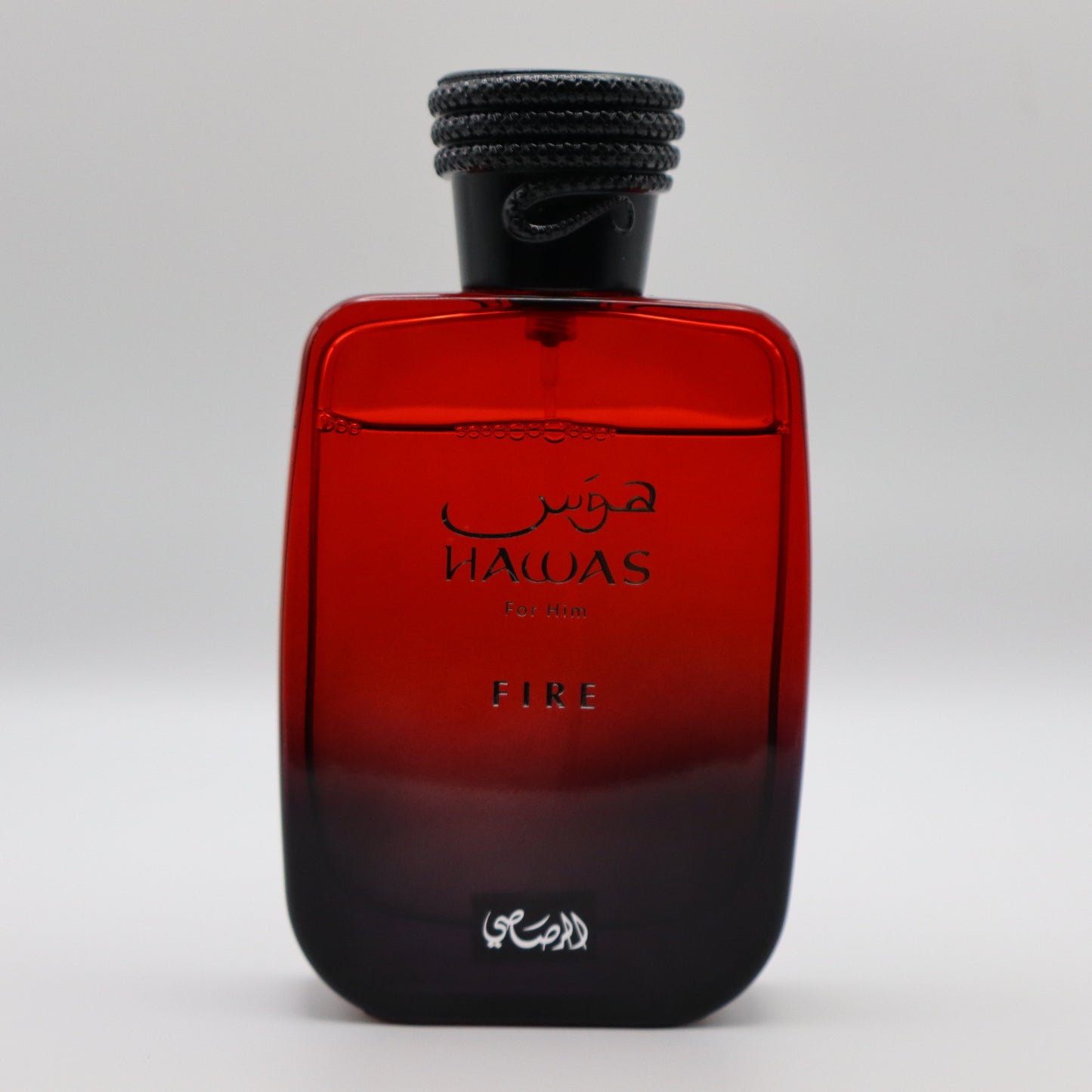 Glass bottle of perfume, transitioning in color from red to black at the bottom. It's labeled 'HAWAS For Him' and 'FIRE' and has a black cap.
