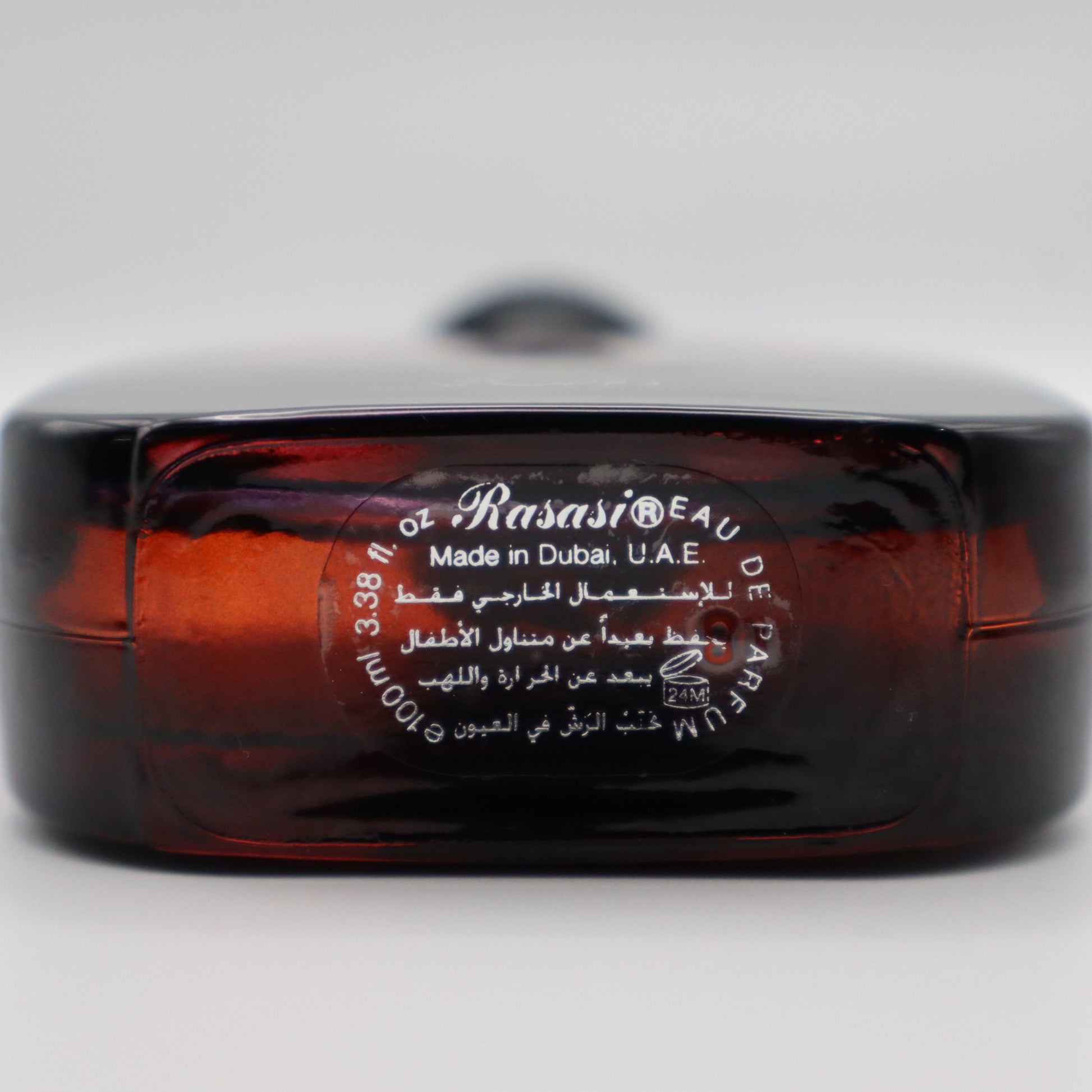 A close-up of a dark red glass bottle with a white printed label reading 'Rasasi' and 'Made in Dubai, U.A.E.'