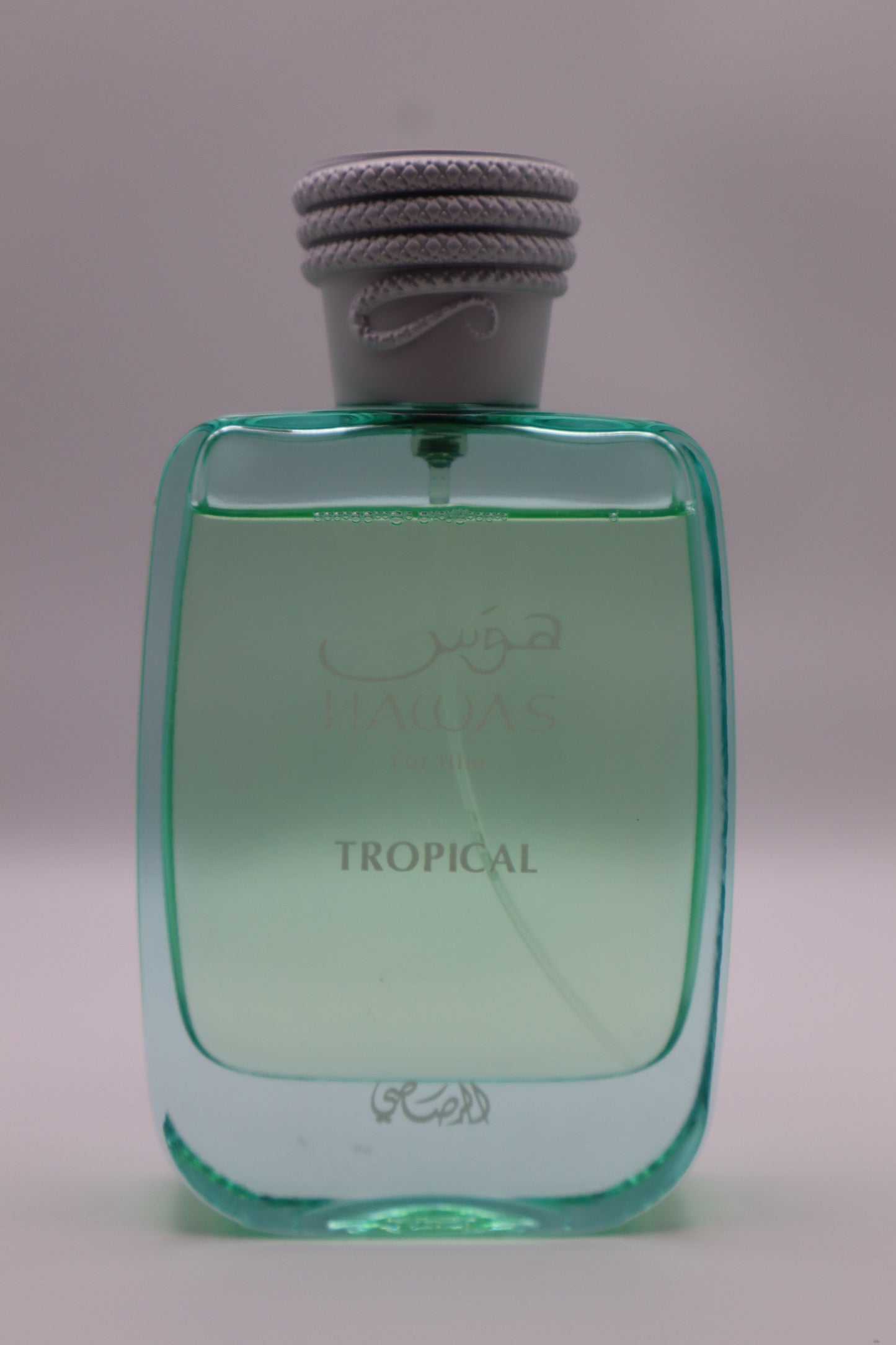 A bottle of Hawas Tropical perfume with a translucent light green body and a gray rope-wrapped cap, set against a plain light gray background.