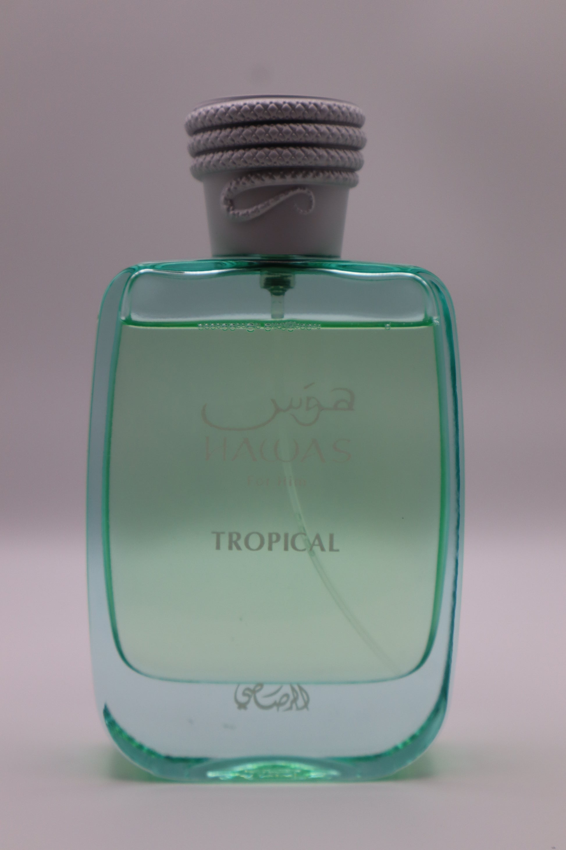 A bottle of Hawas Tropical perfume with a translucent light green body and a gray rope-wrapped cap, set against a plain light gray background.