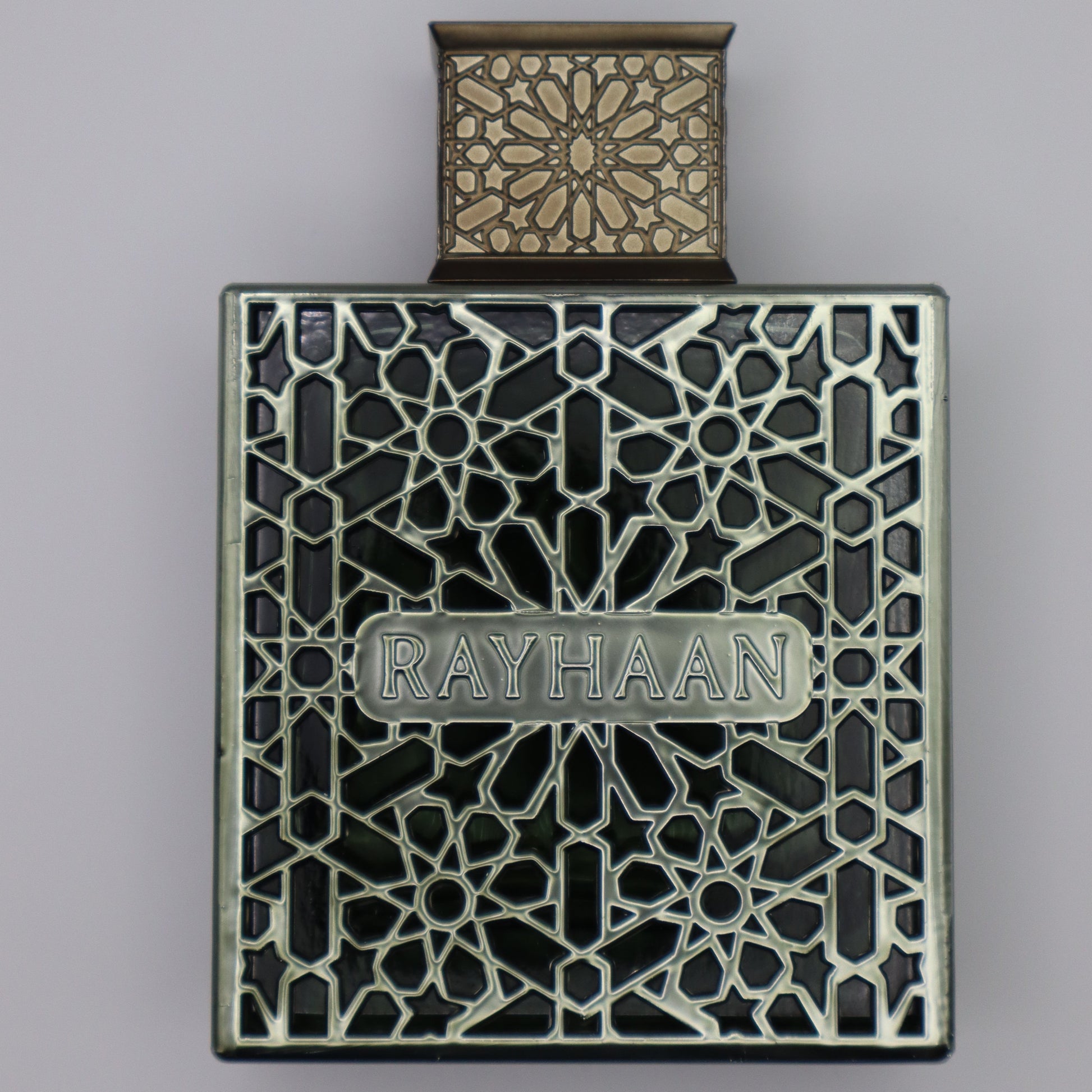 Perfume bottle in a slightly gold color and an intricate geometric design with the label 'RAYHAAN'